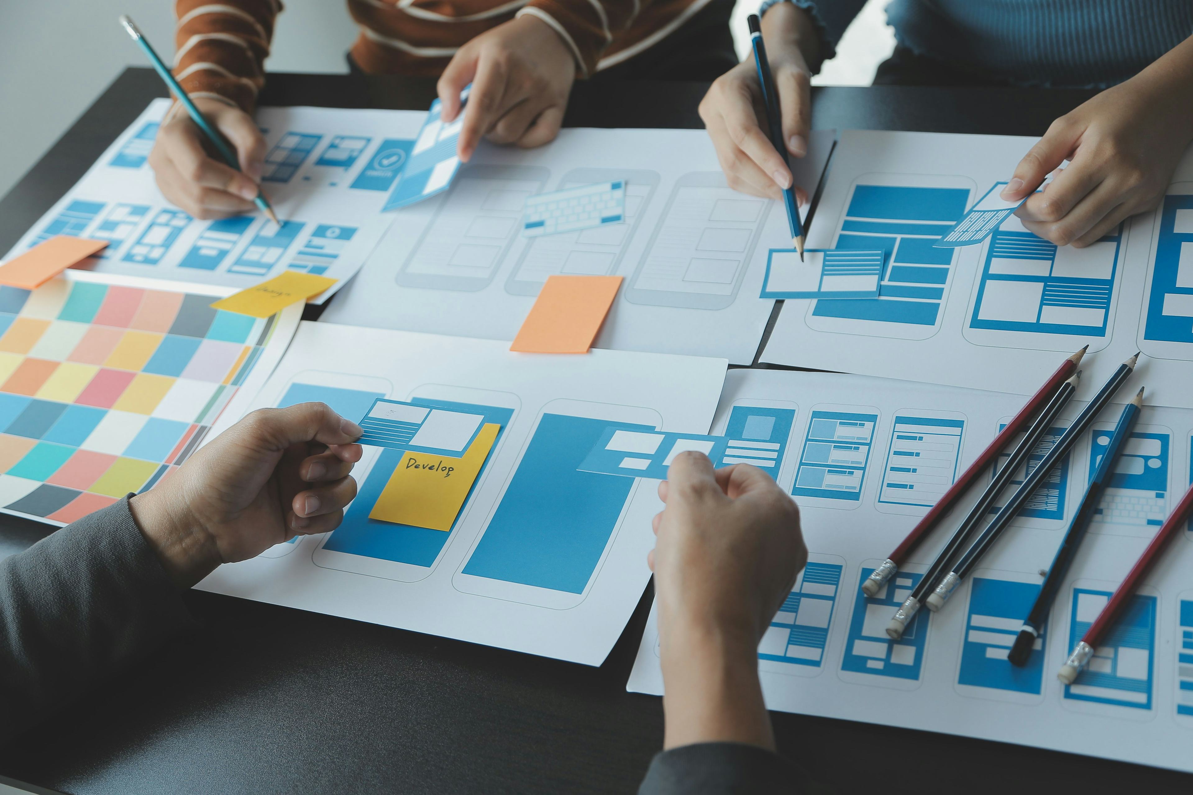 Close up ux developer and ui designer brainstorming about mobile app interface wireframe design on table with customer breif and color code at modern office, Creative digital development agency