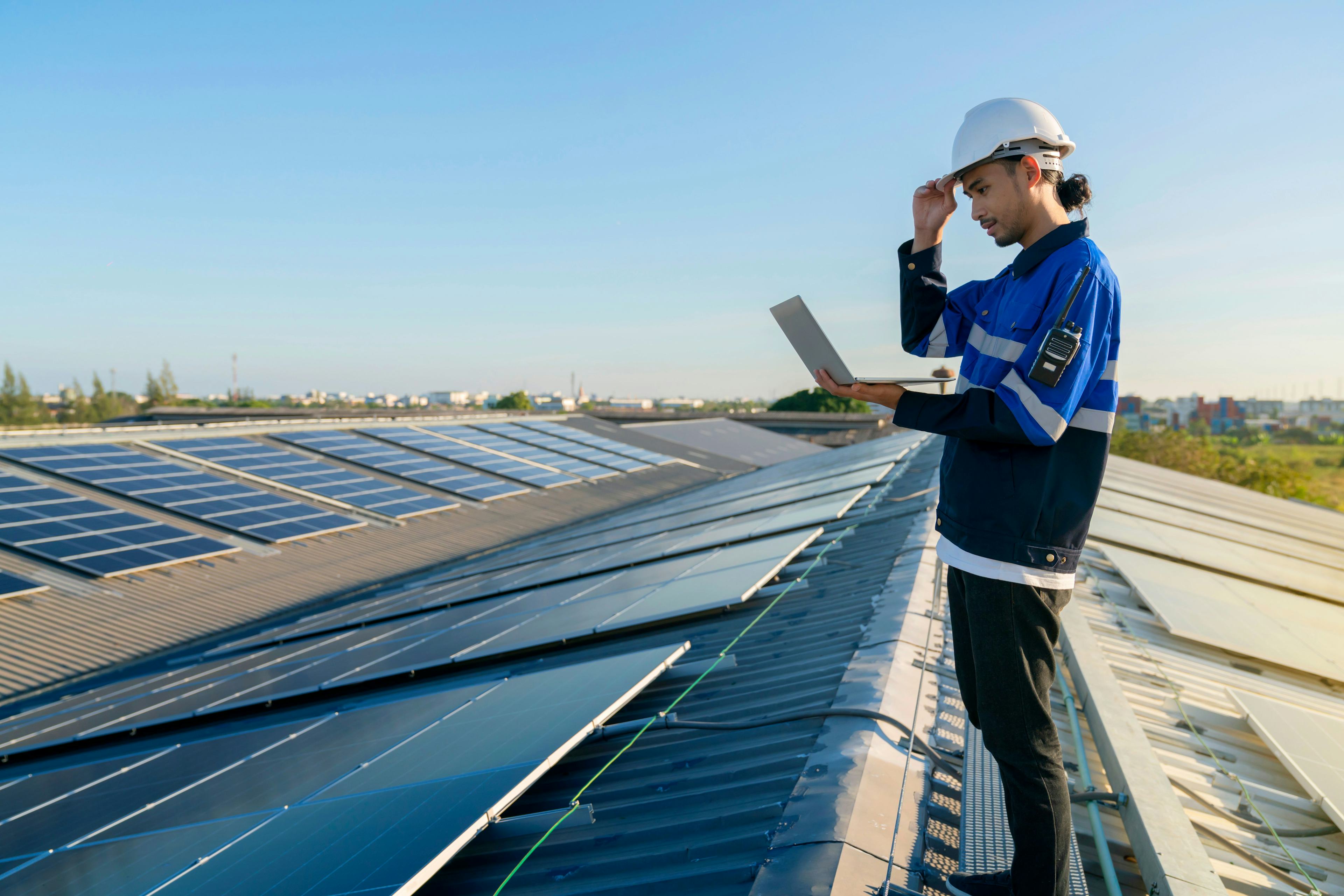 person holding an open laptop while inspecting solar panels