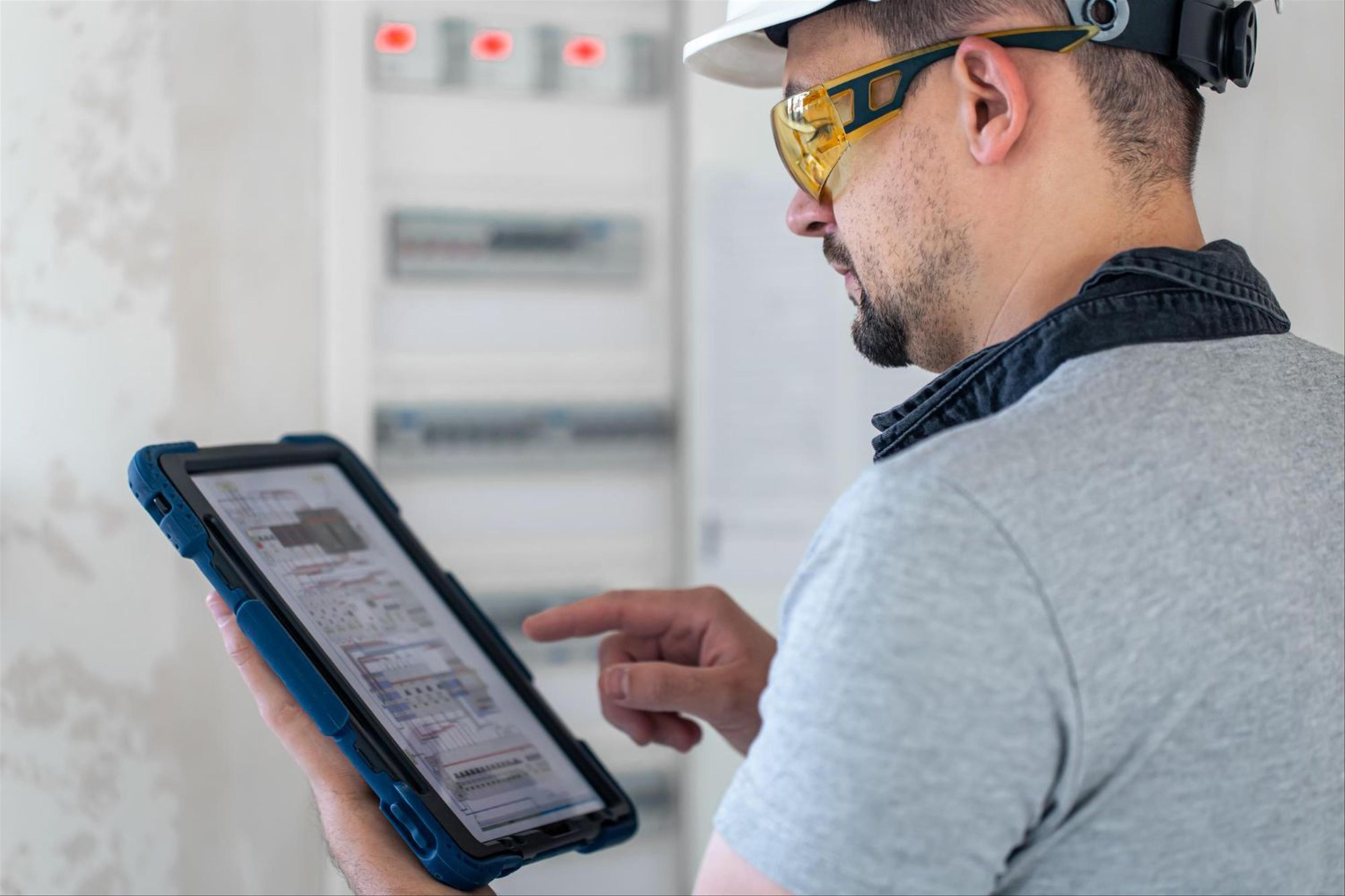 man with hard hat handling tablet with management system