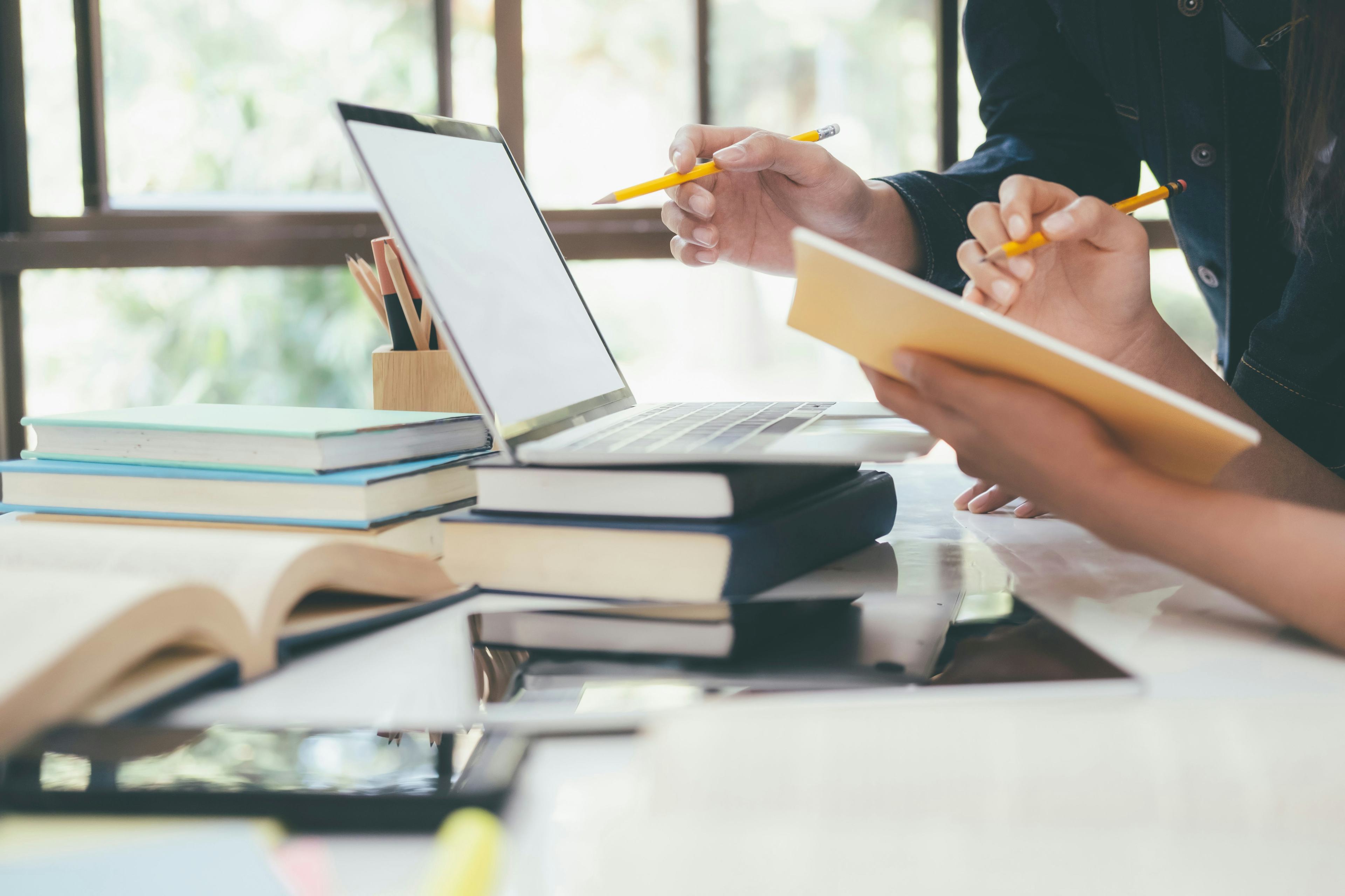 side view of students studying on laptop surrounded by books