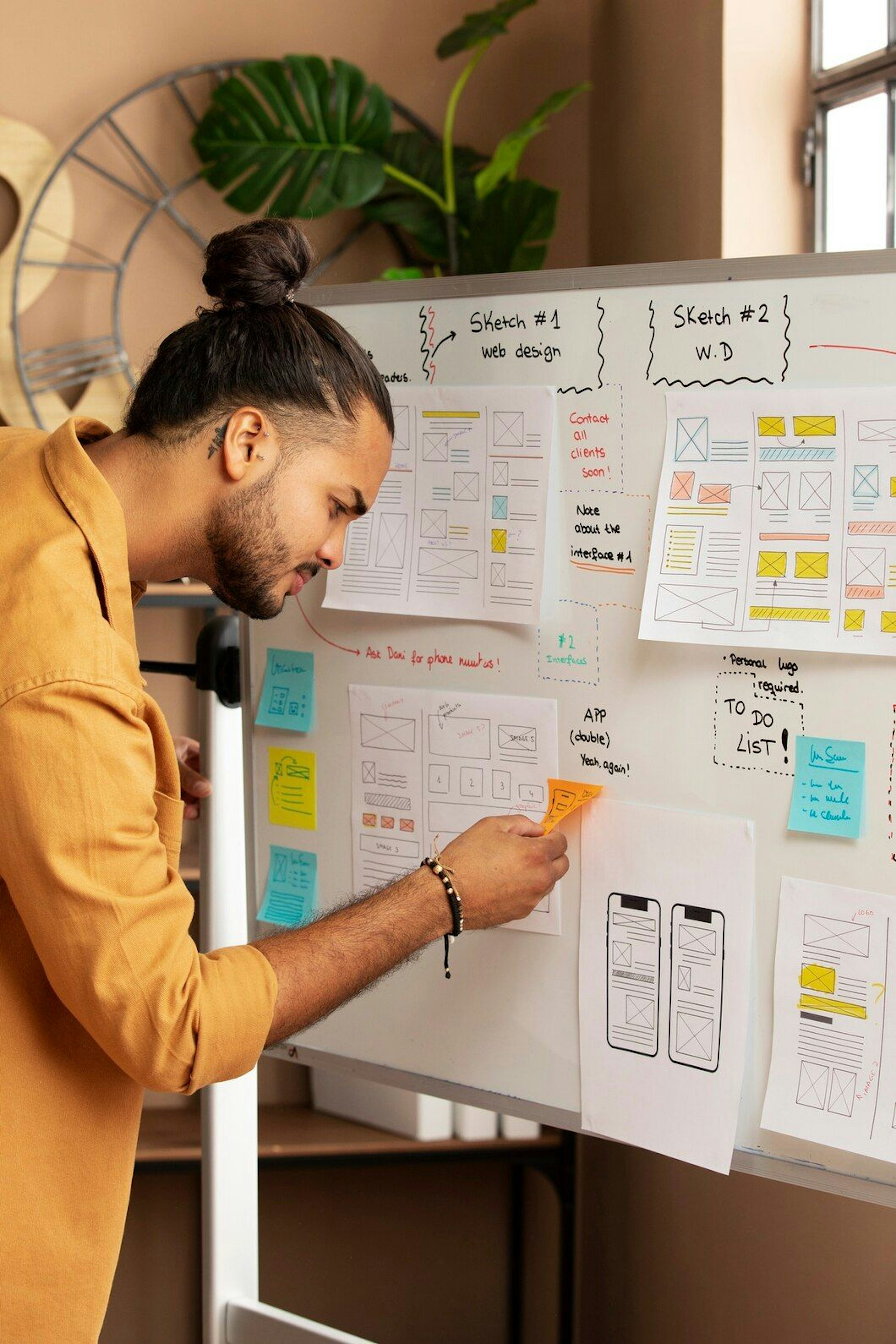 male web designer with several user interface designs for mobile phone apps on a board