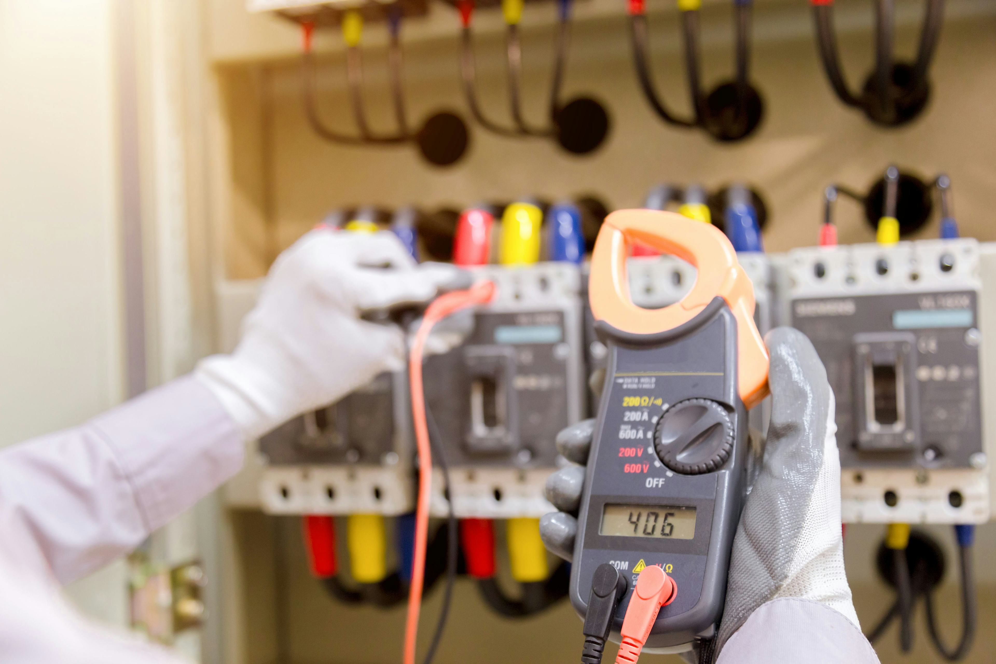 Technician measuring voltage or current by voltmeter in control panel