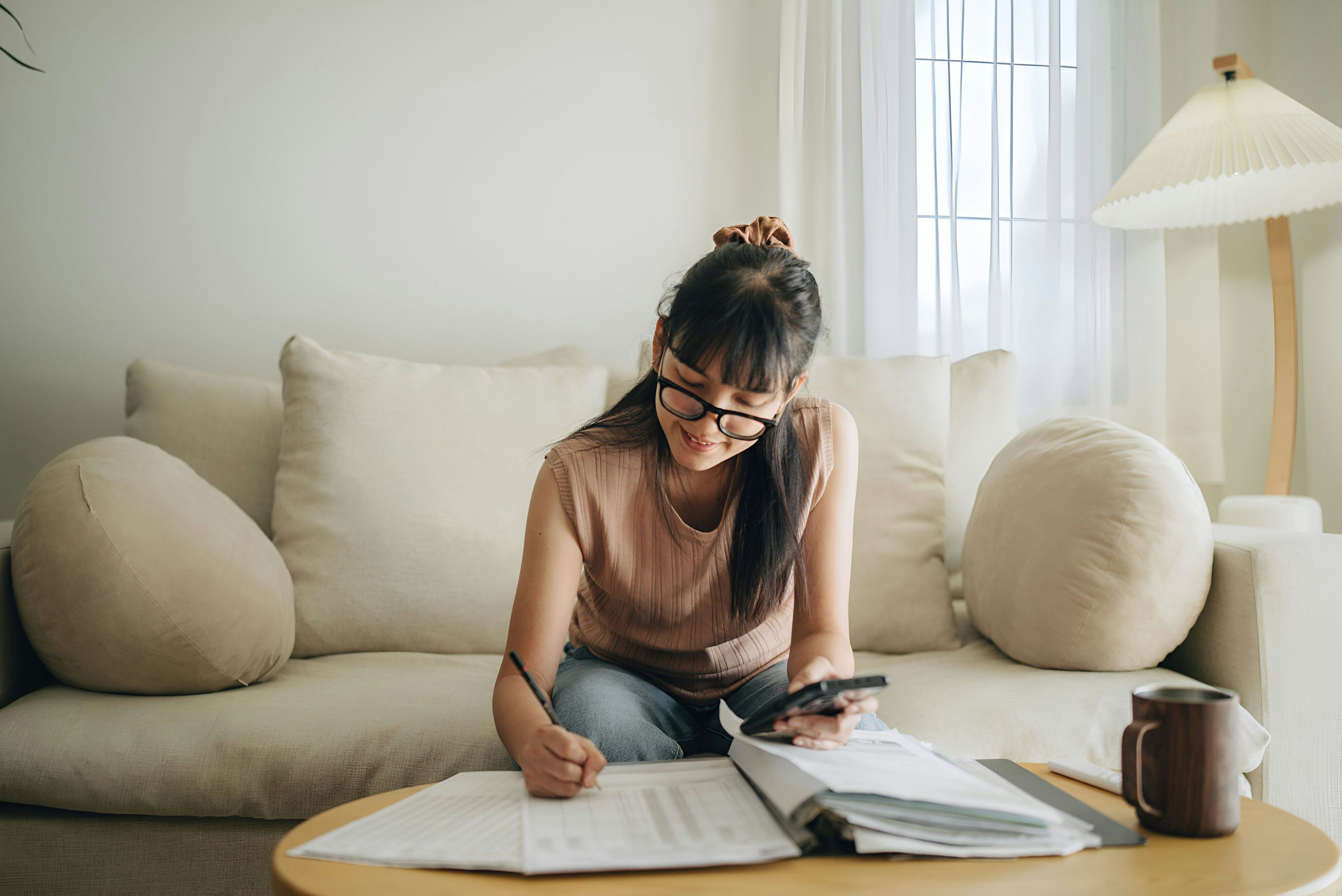 woman wearing glasses holding phone and writing something down on paper