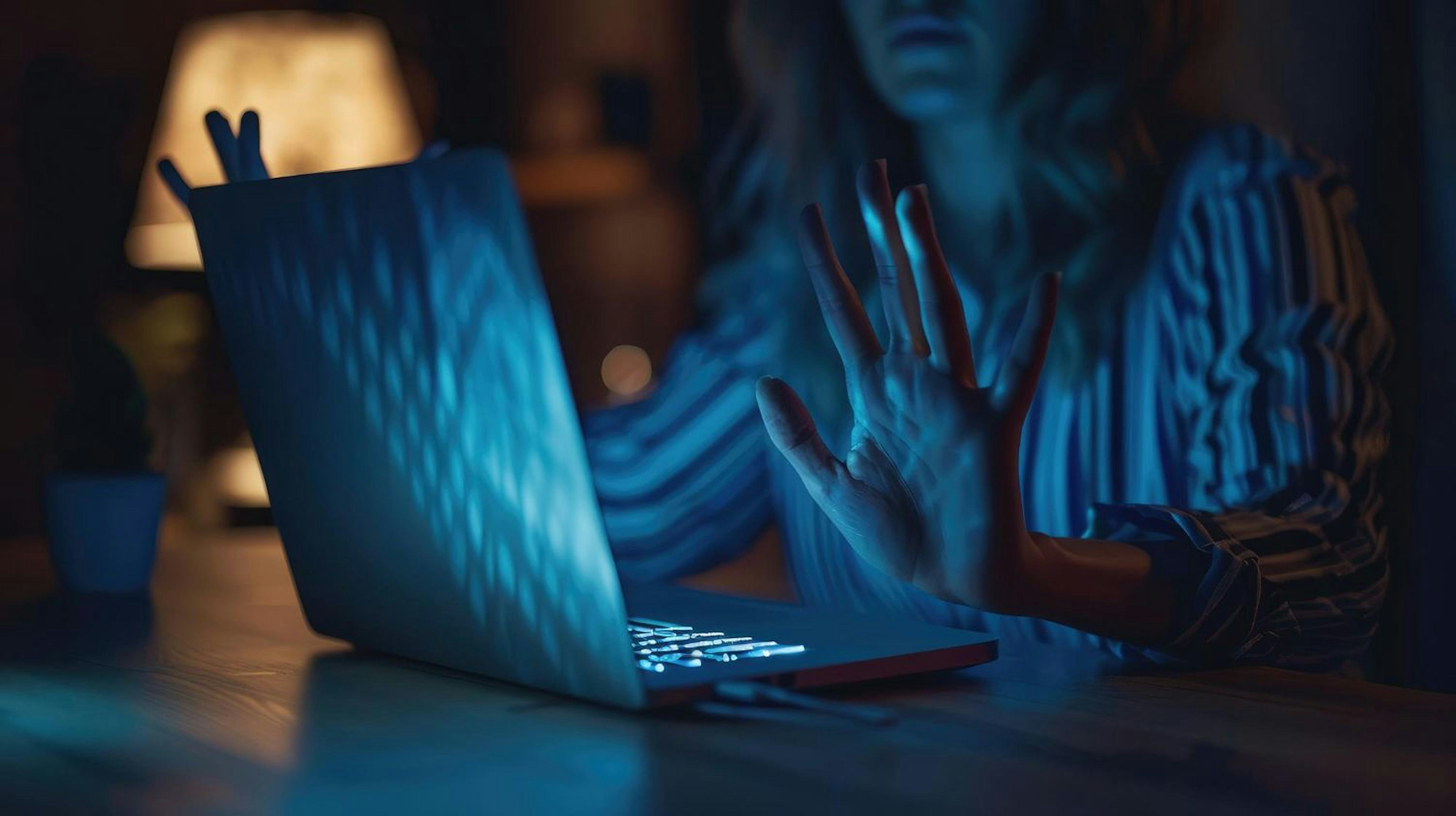 A person sitting at a desk with their hands together in front of an open laptop