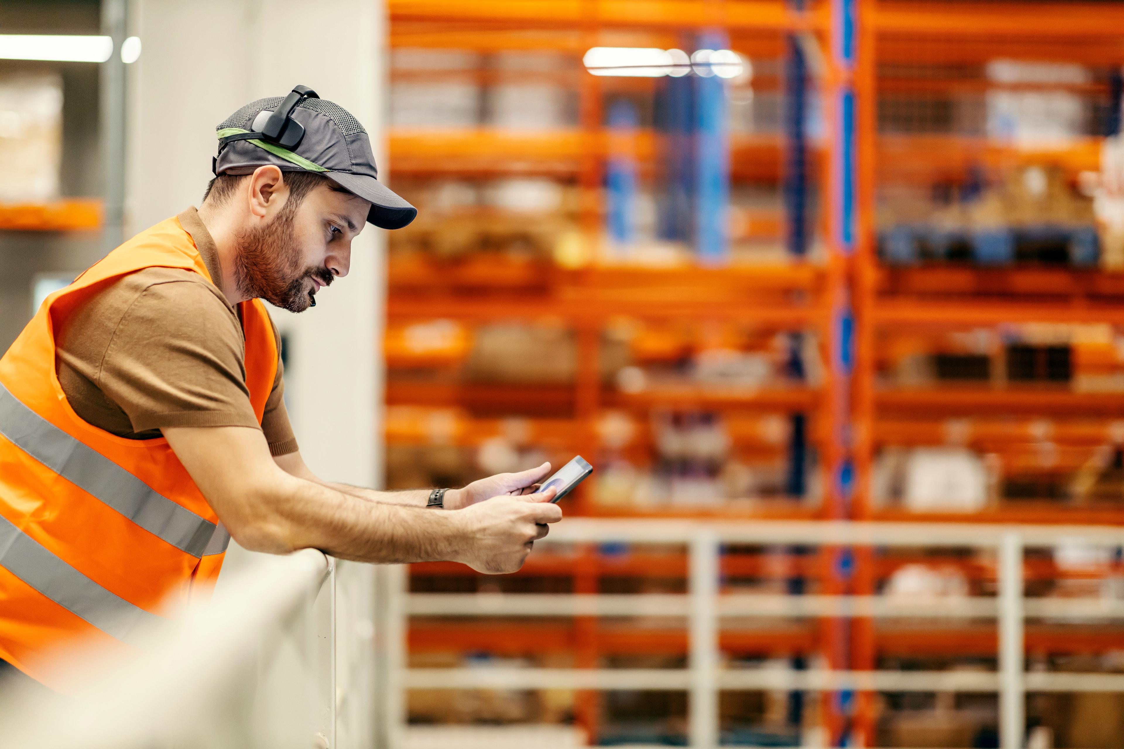 man working in storage warehouse while holding and viewing info on tablet