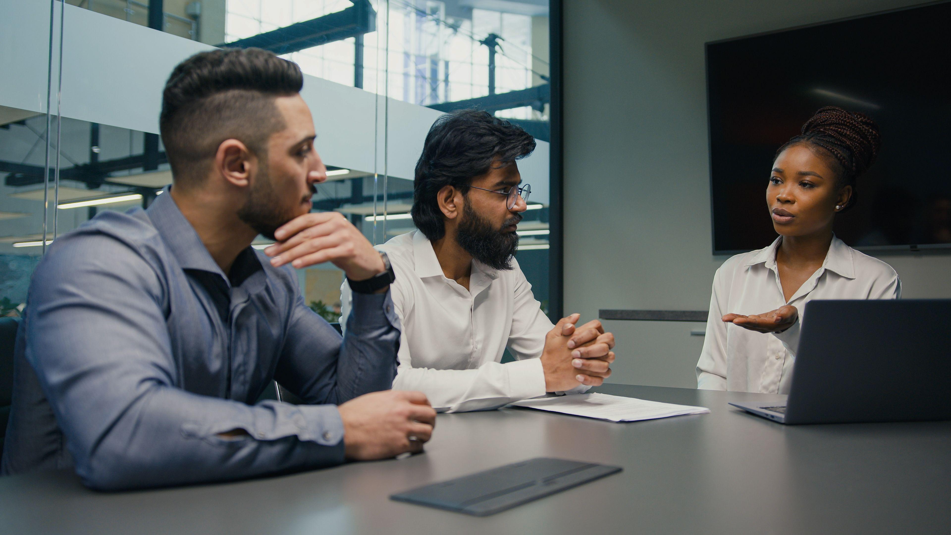 woman and two men conversing over business matters at a conference table in a glass room