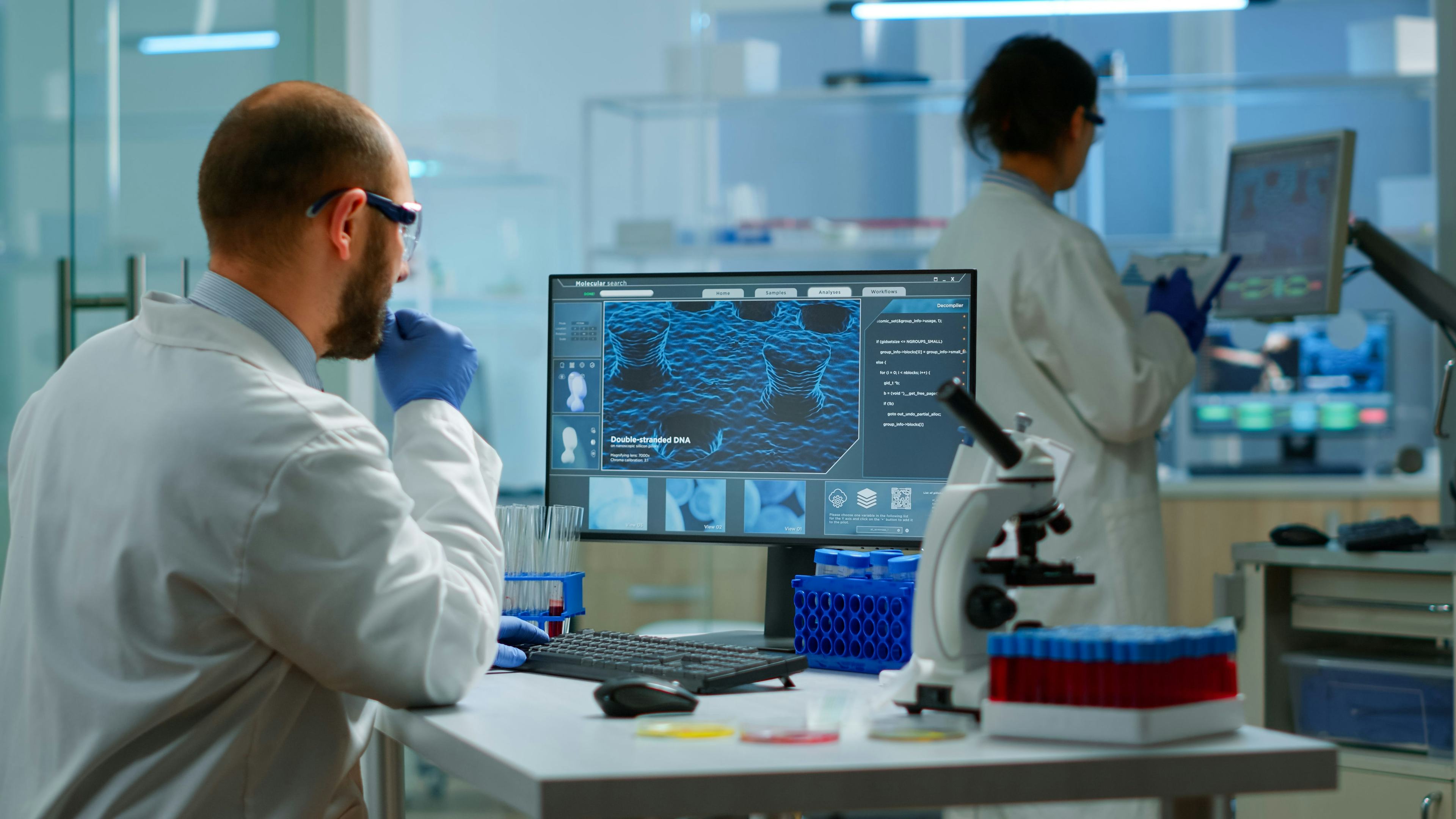 man in white coat in lab viewing information on computer