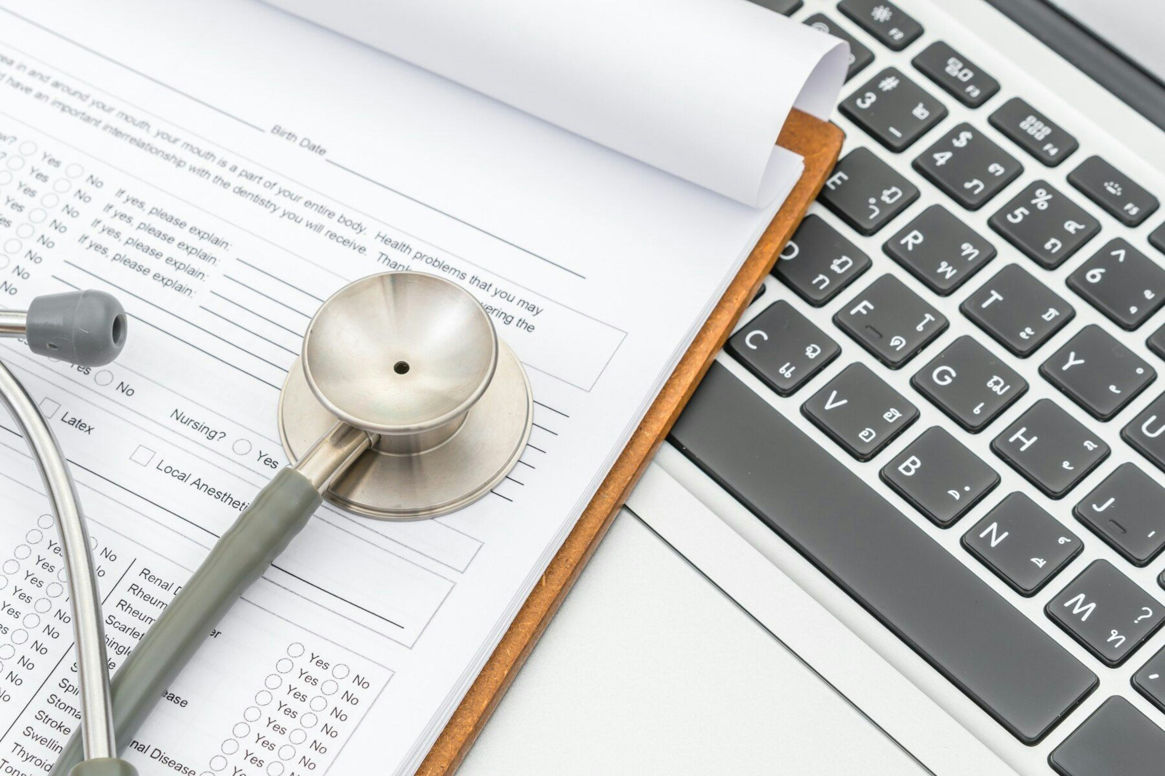 Stethoscope on a clipboard with patient medical form on top of laptop keyboard