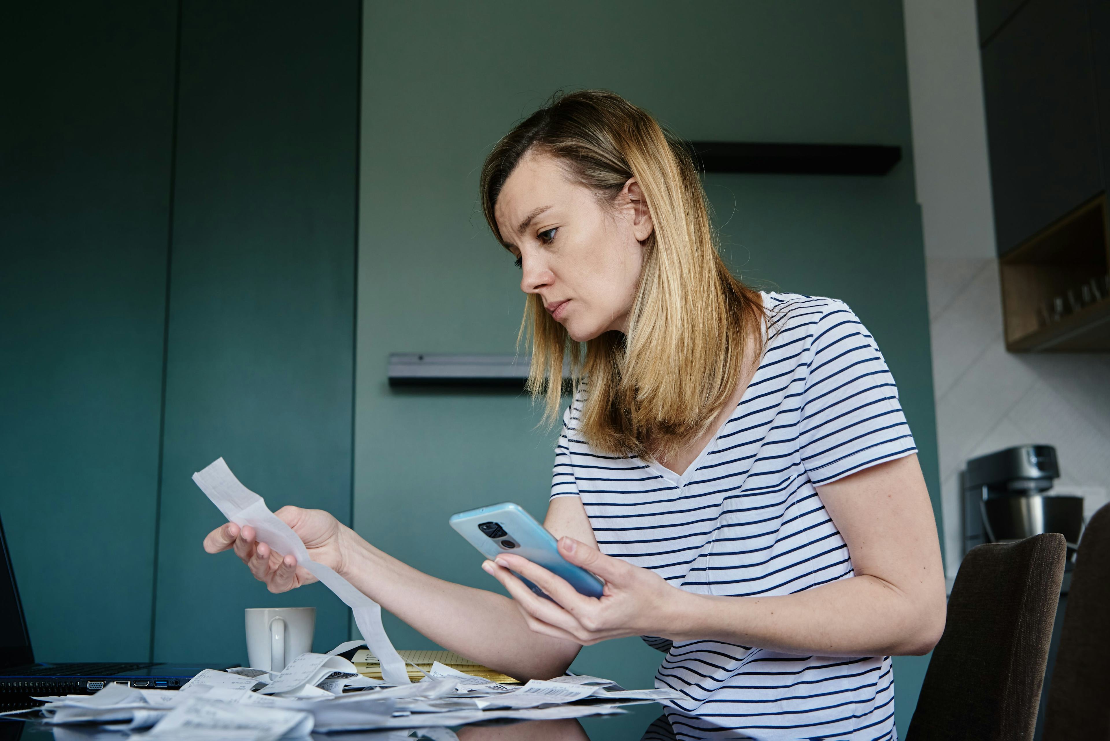 woman recording expenses on application on phone while holding a long receipt