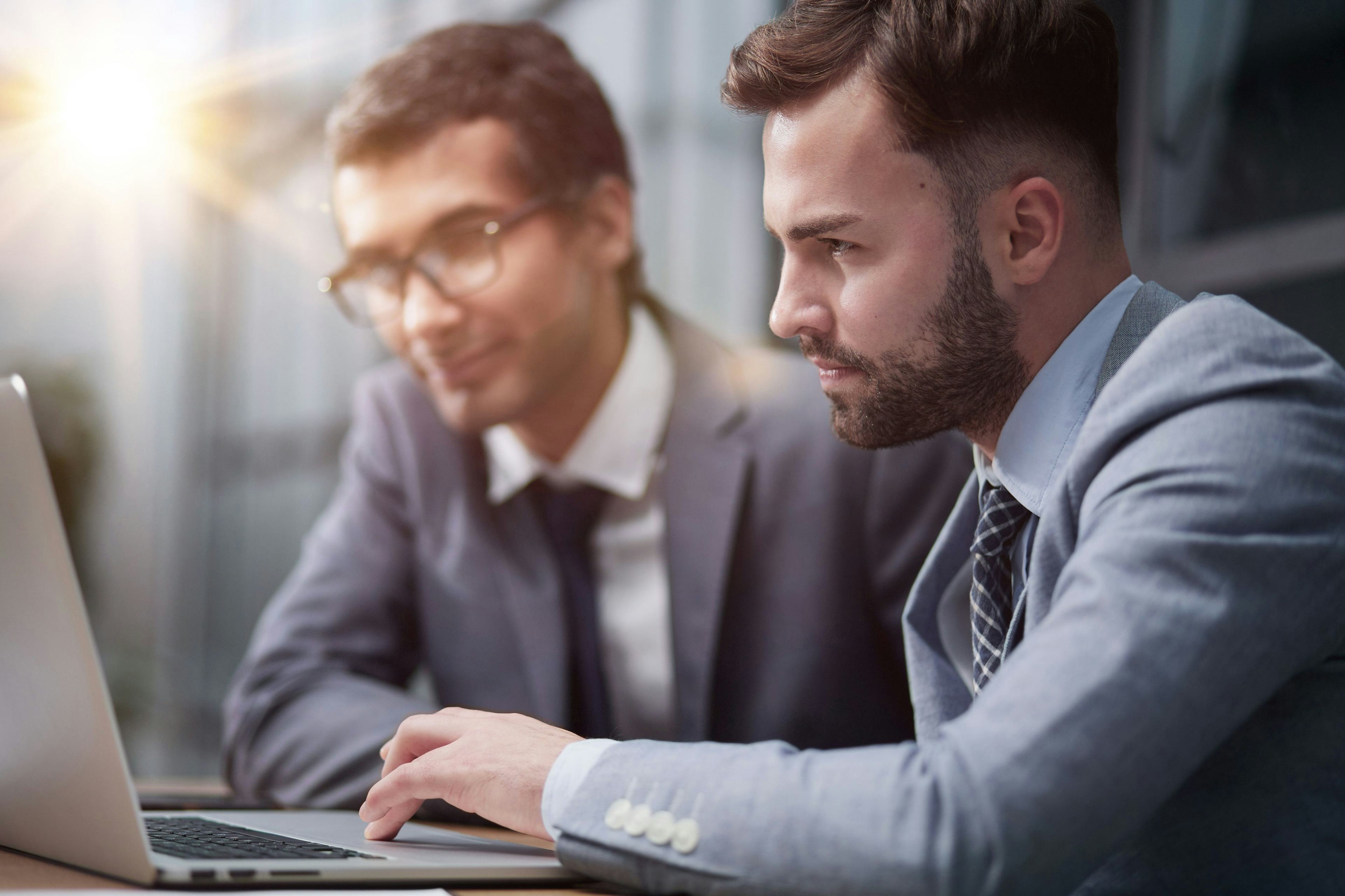 Two young businessmen sitting at workplace and working together in office