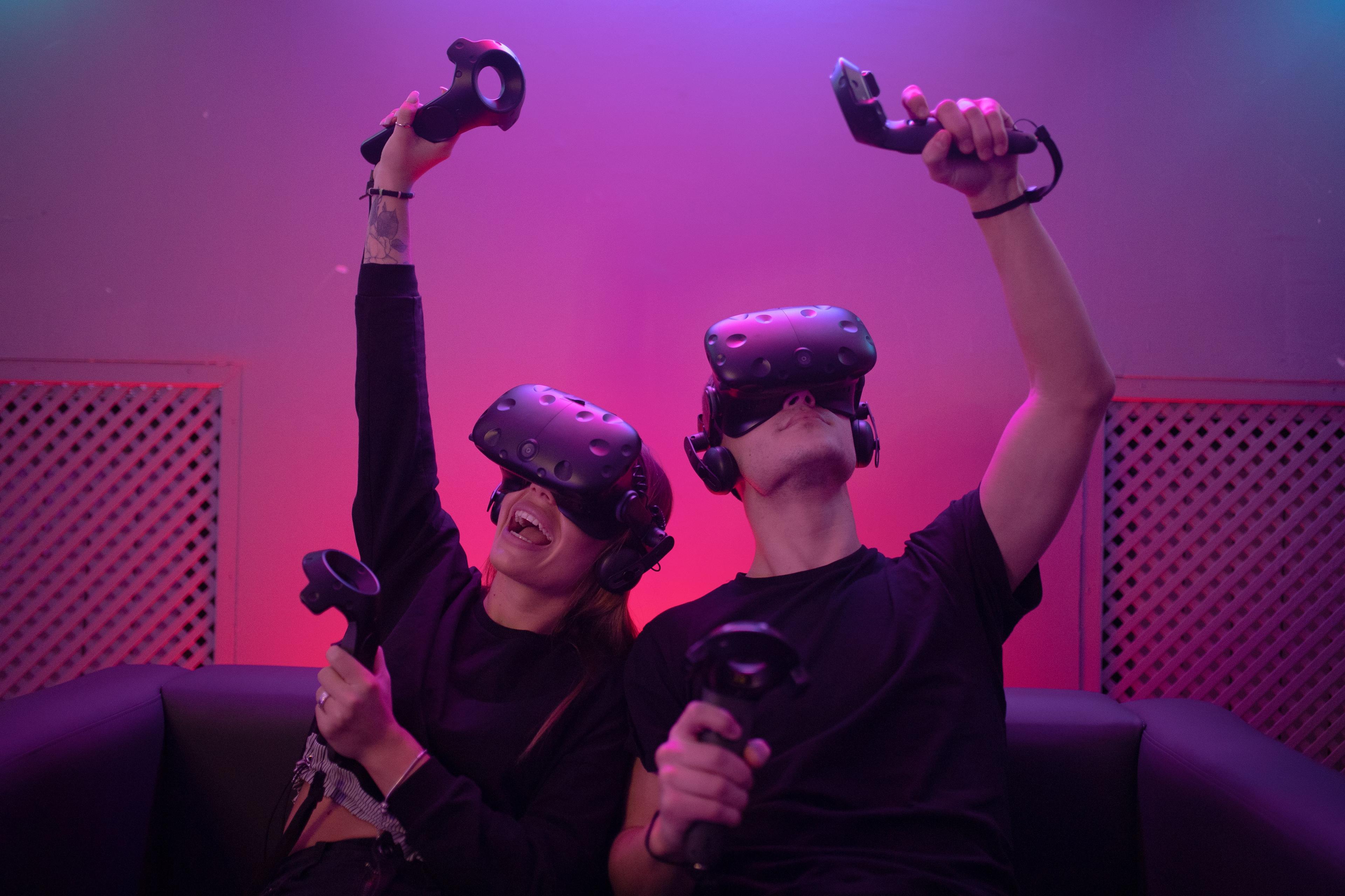 A young woman and man lifting their arms in the air while playing virtual reality.