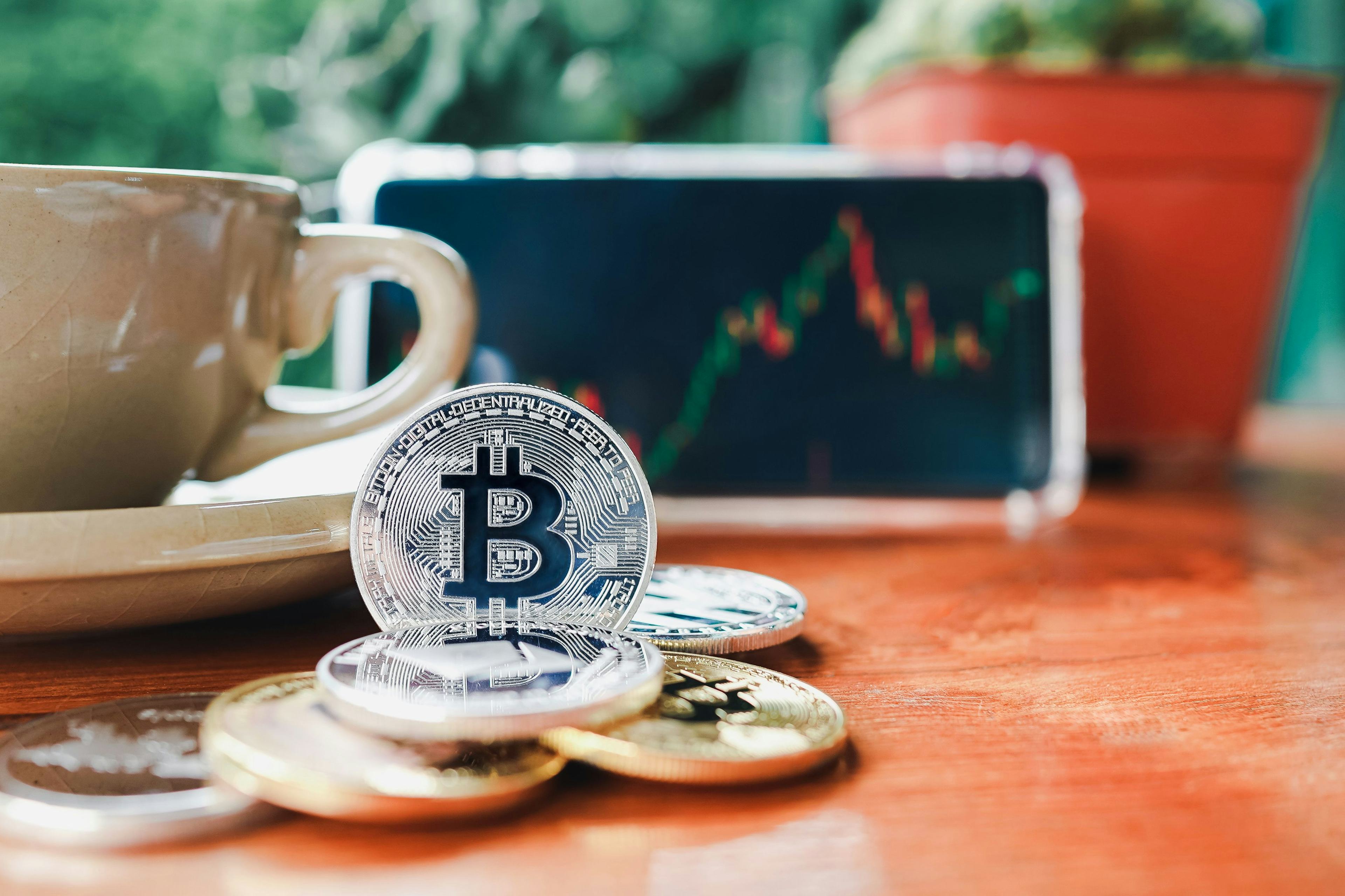 pile of bitcoin siting on a desk in front of a coffee cup and phone