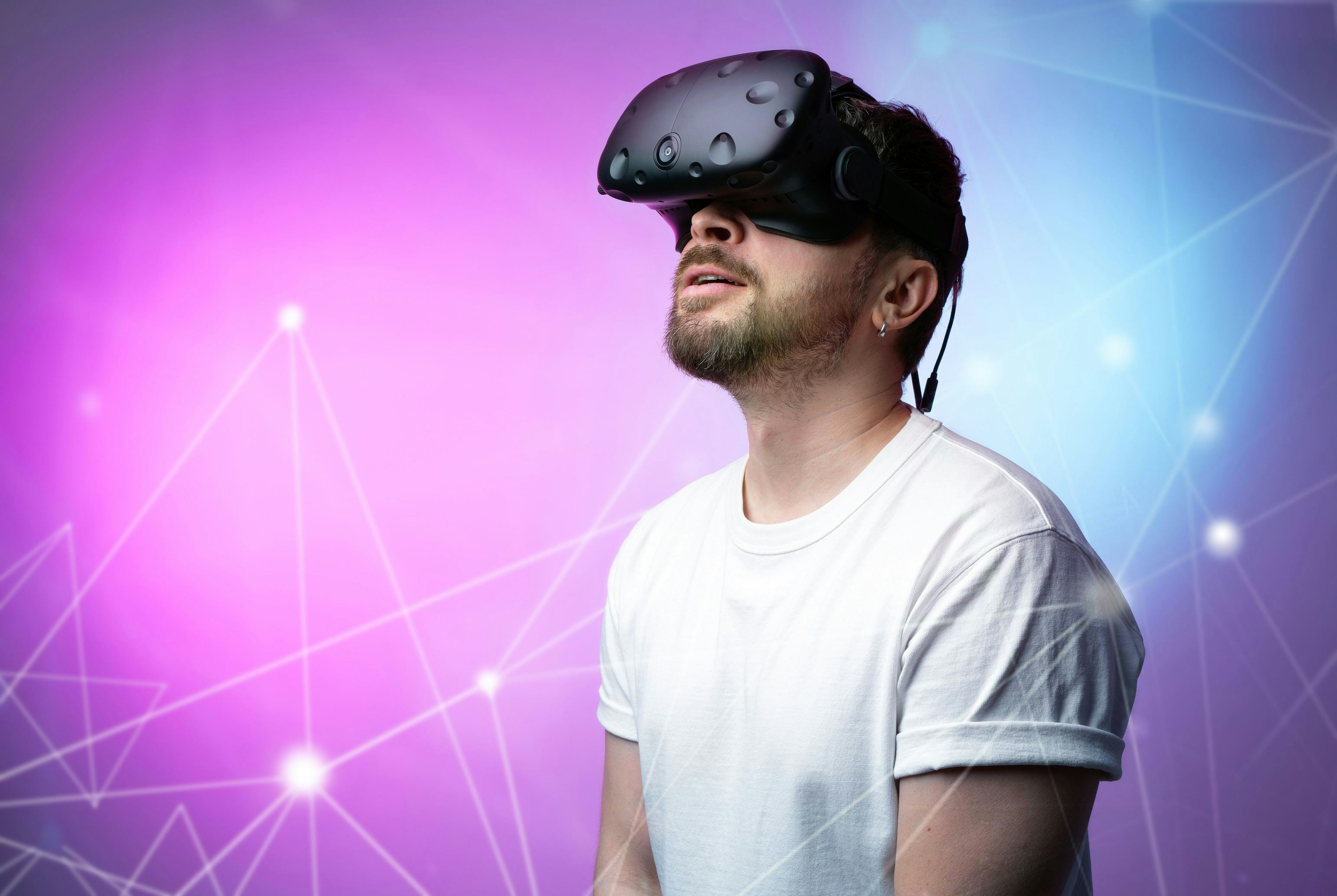 A guy with a VR headset on standing in front of purple and blue graphics