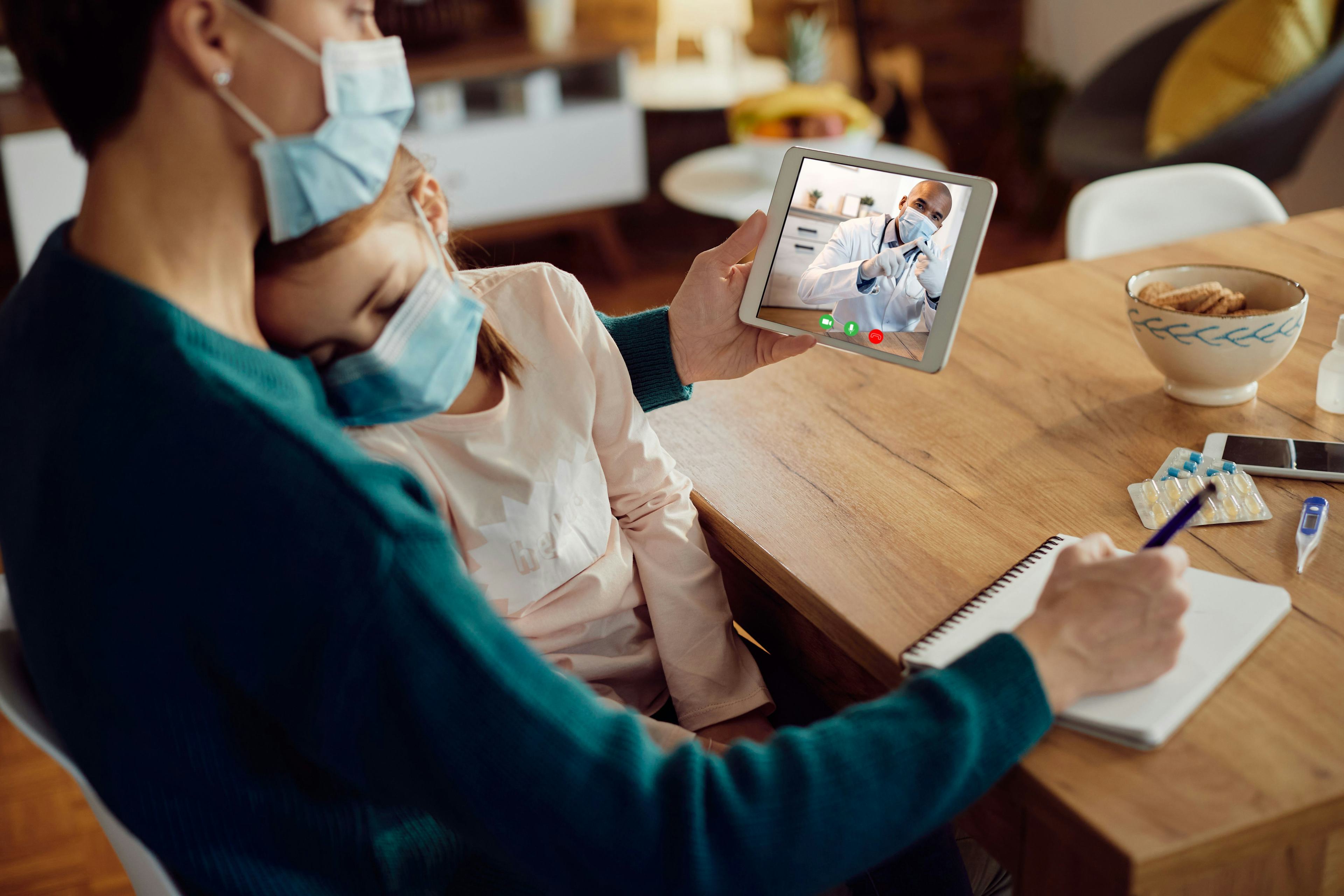 mother and sick child wearing masks meeting with doctor over video call