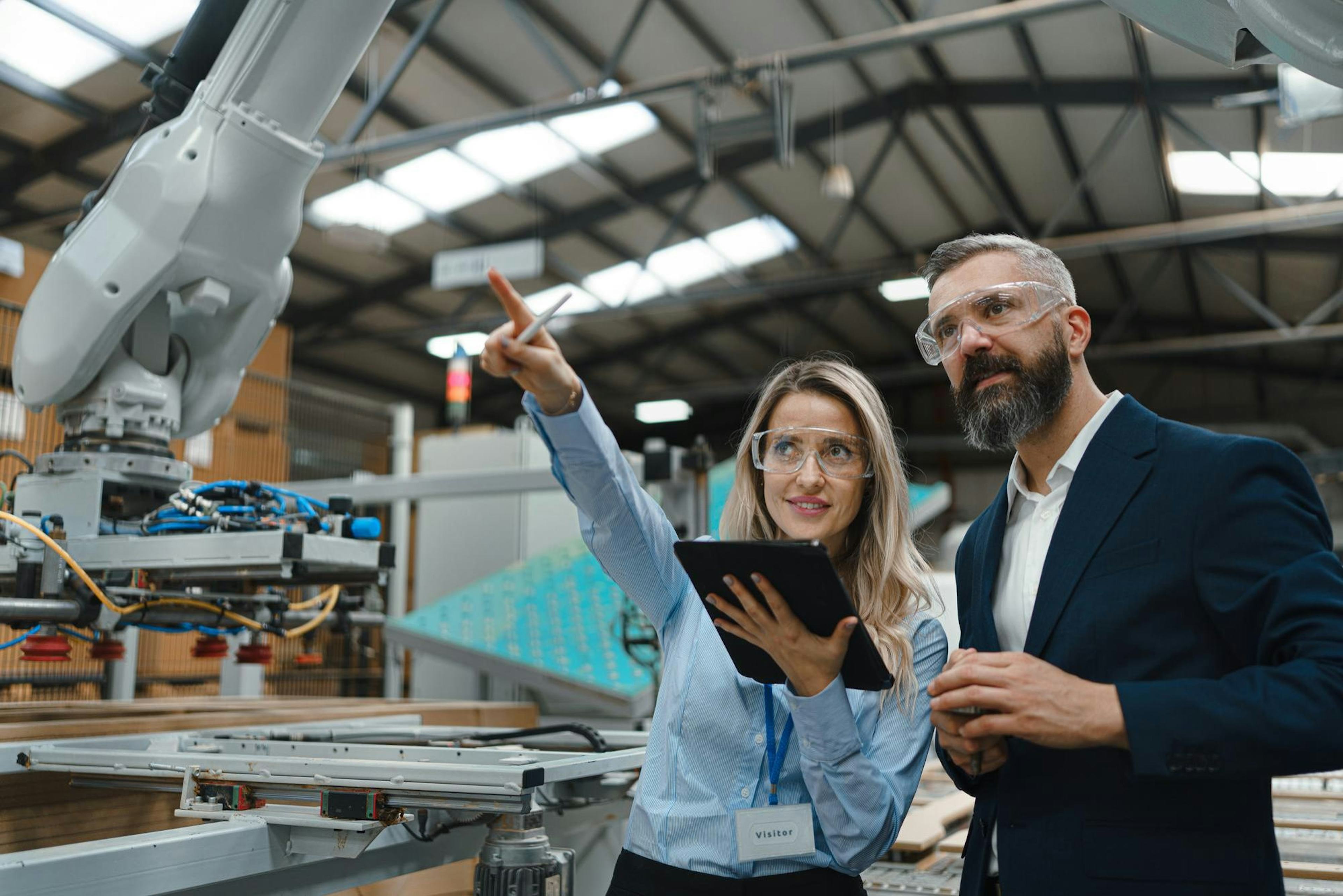 two professionals looking at an industrial robotic arm while wearing clear goggles