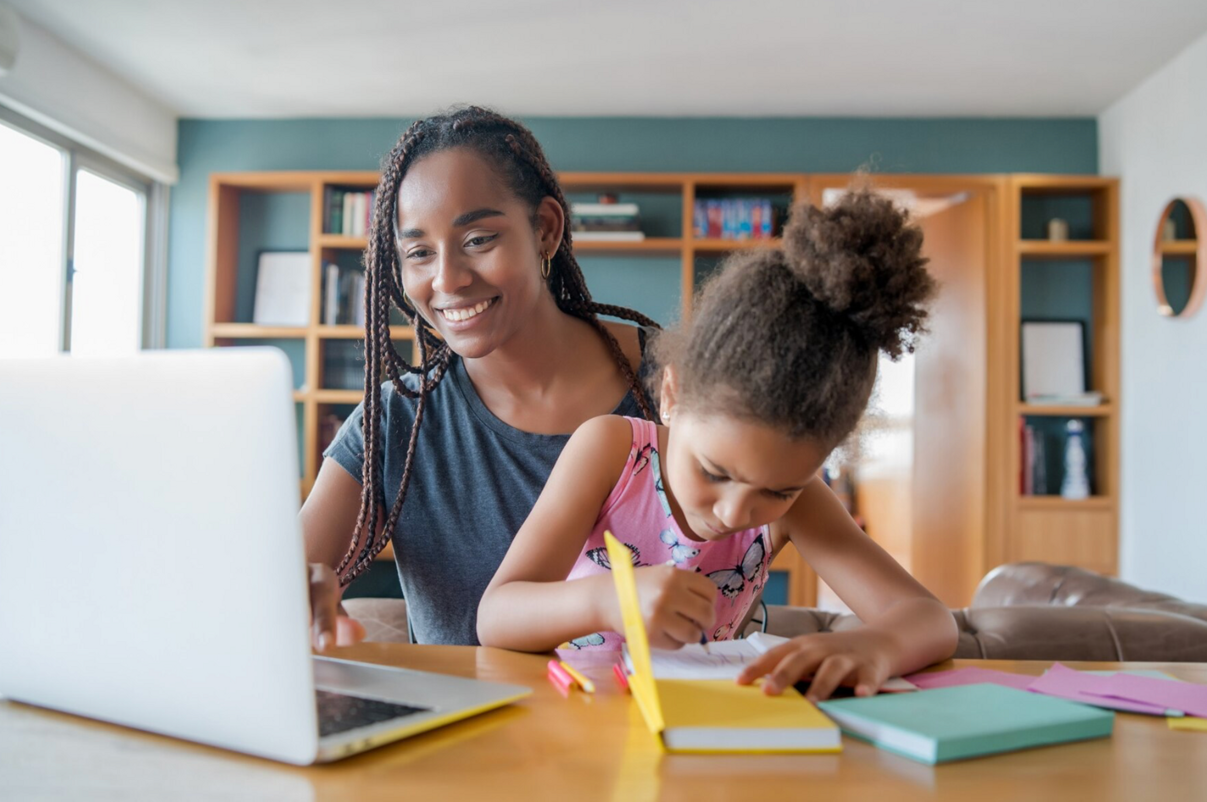 mother helping young daughter with schoolwork on laptop at home