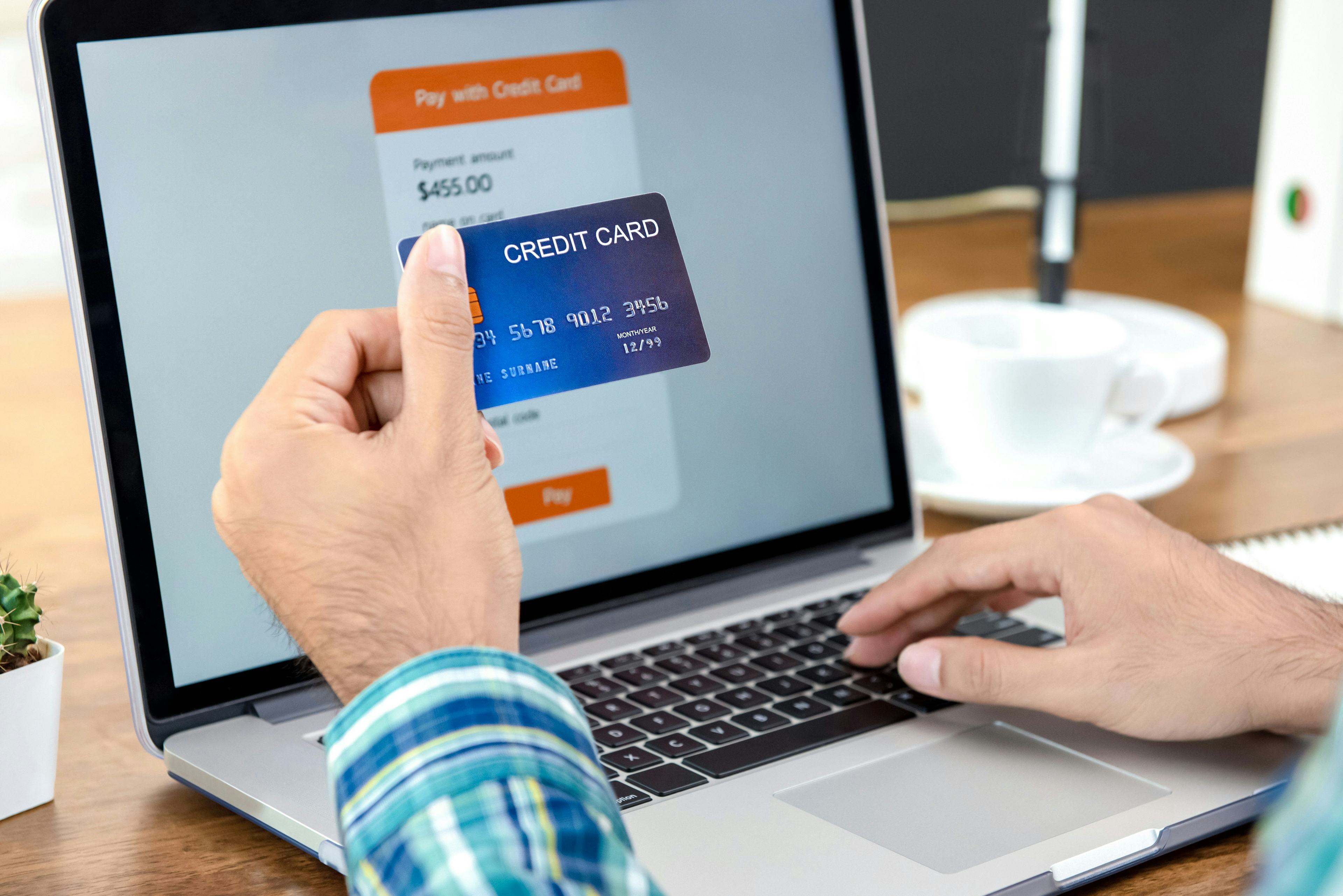 man holding a credit hard with financial info in backdrop on computer screen