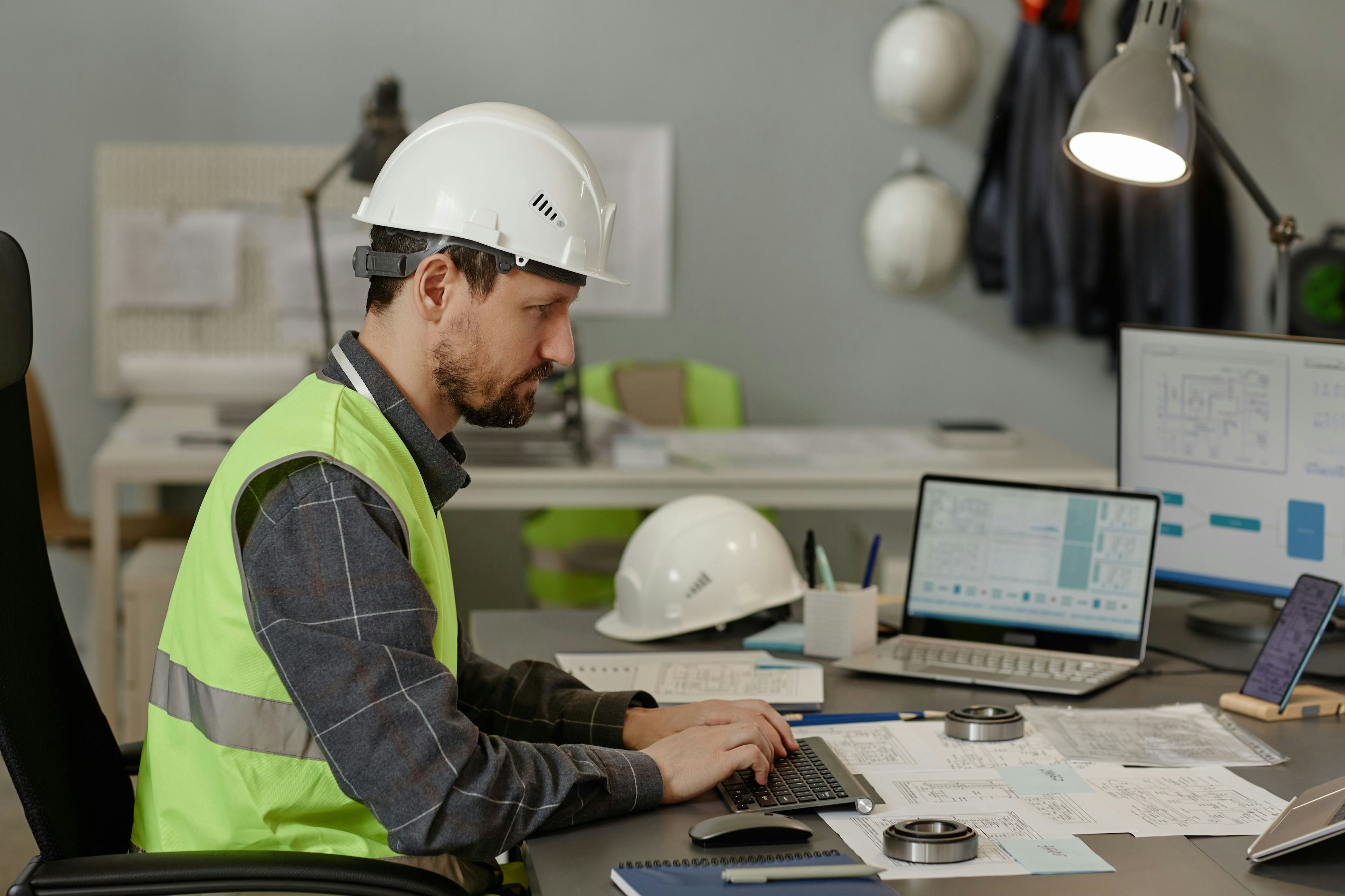 Engineer wearing hardhat at workplace in office and using computer devices