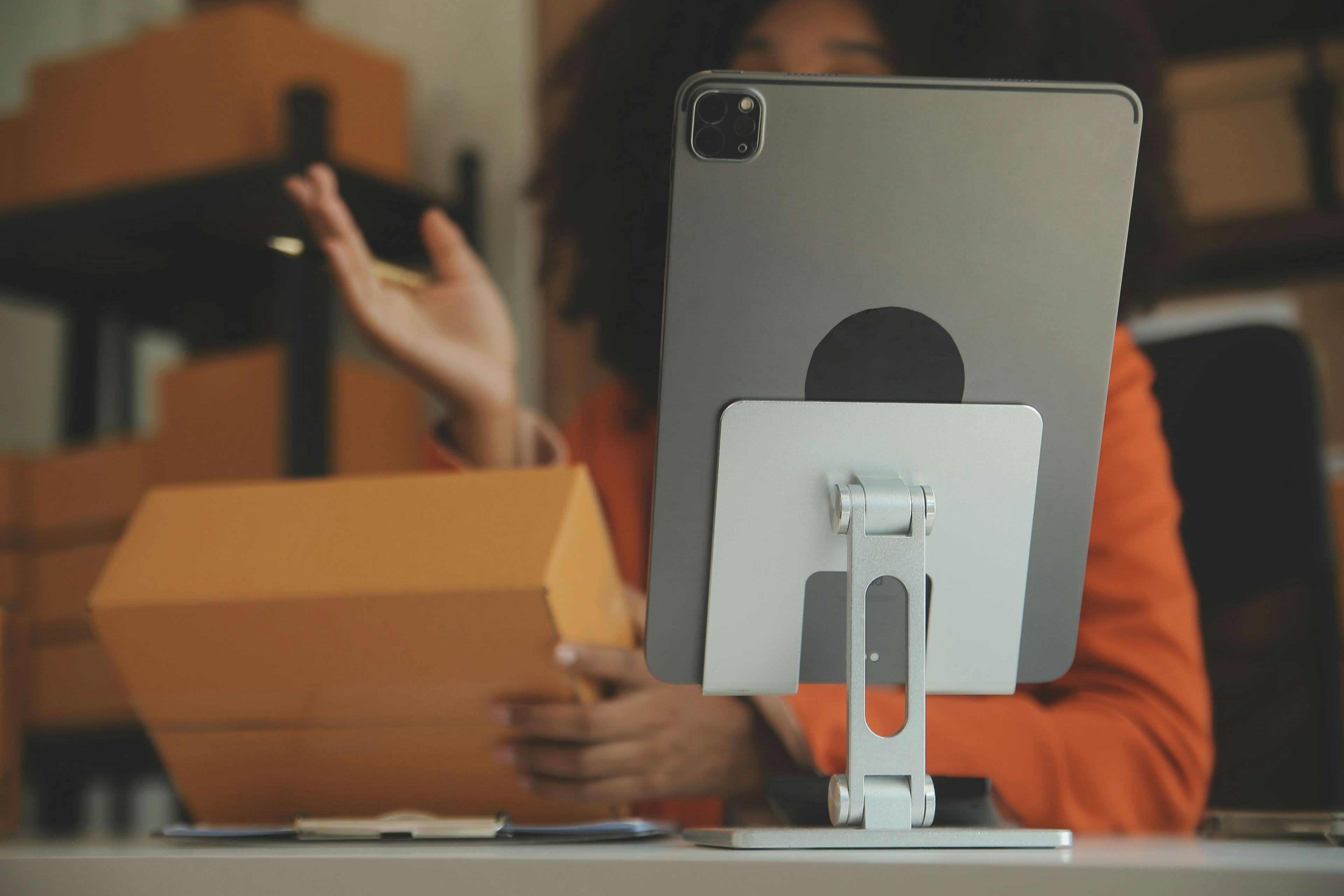 tablet on a stand while a person sits behind it holding a cardboard packaged product