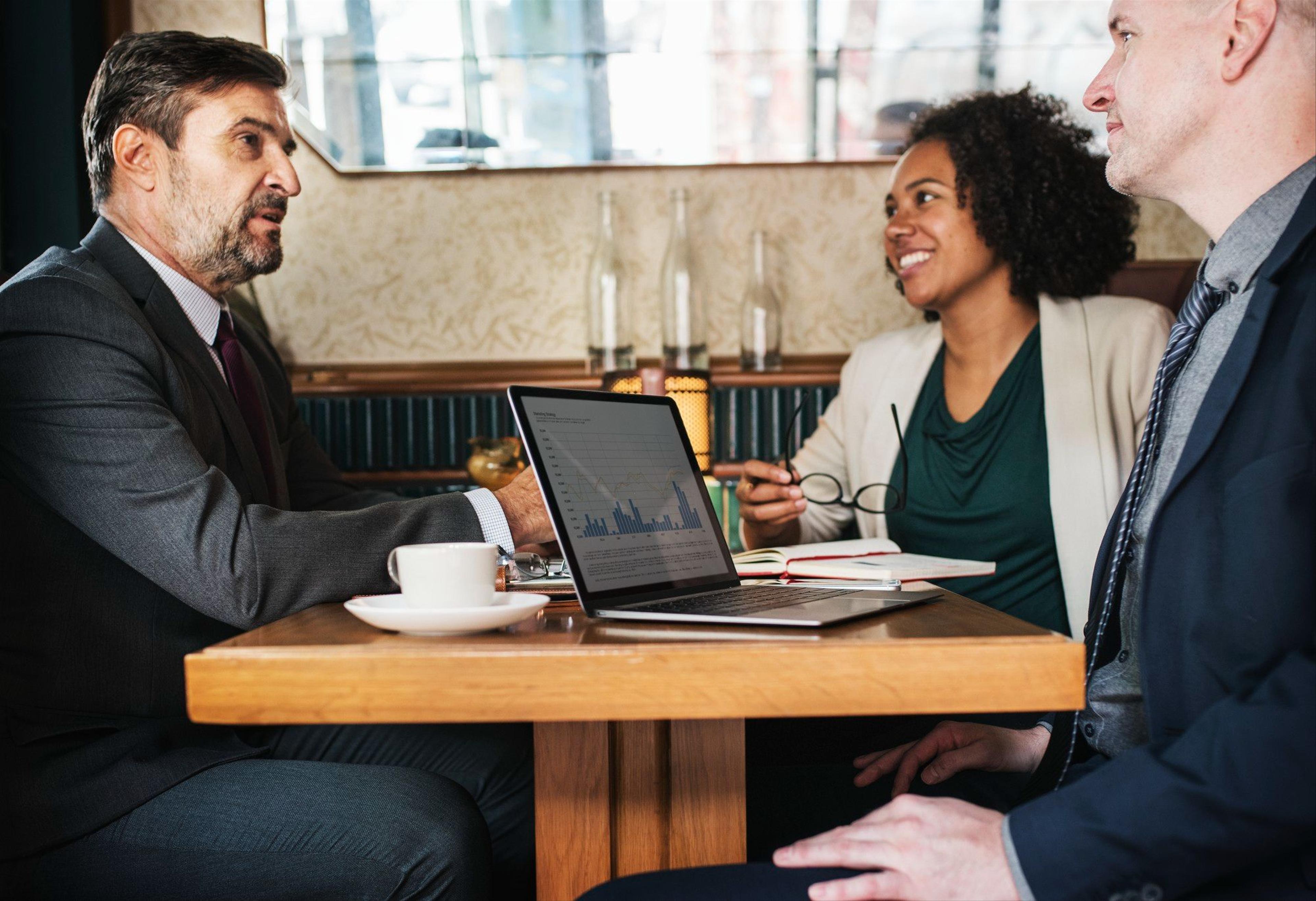 business meeting with three people at a table with a laptop open