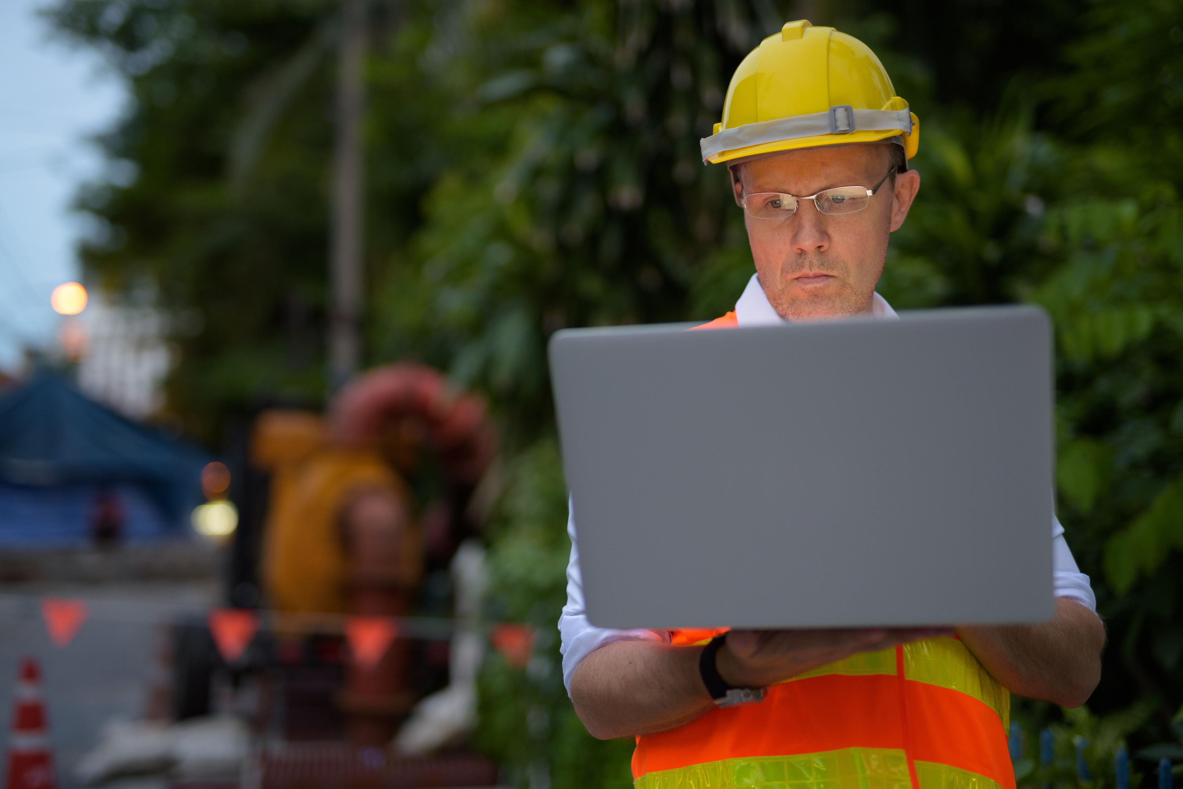 utility worker wearing hardhat working on open laptop