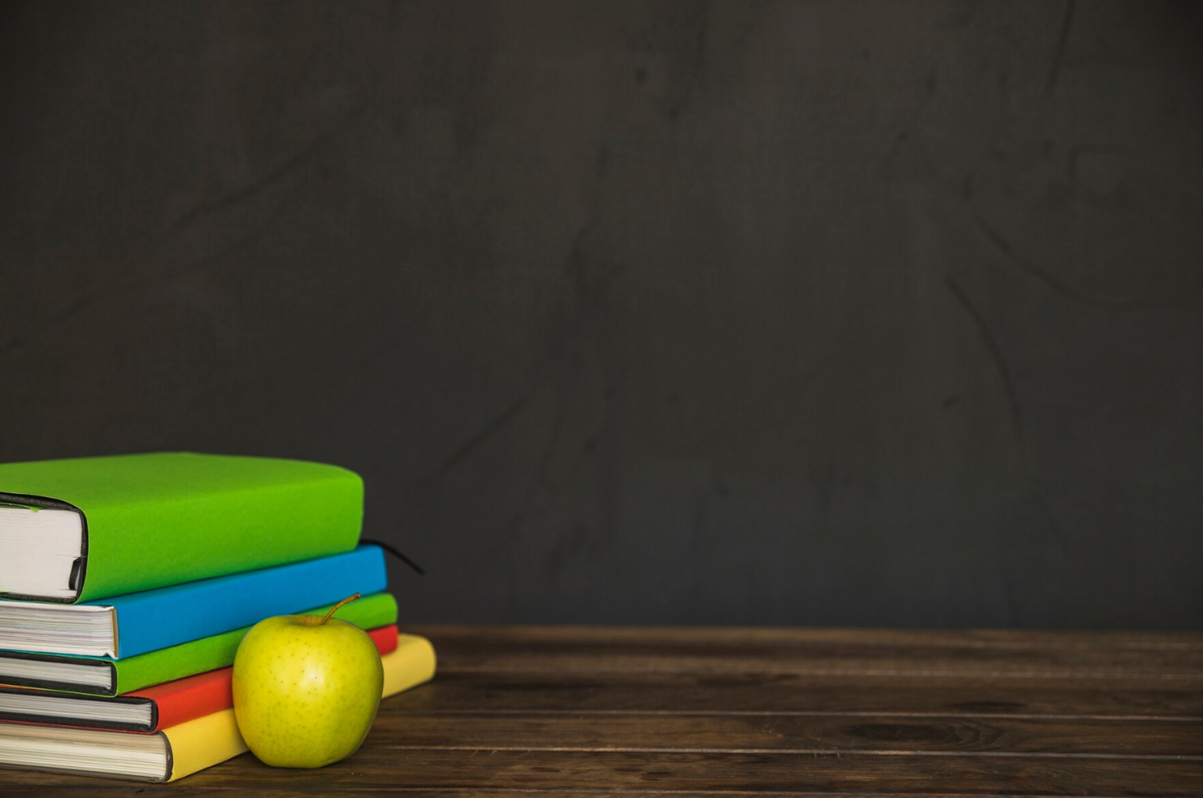 pile of books on table with apple in front and blackboard in background